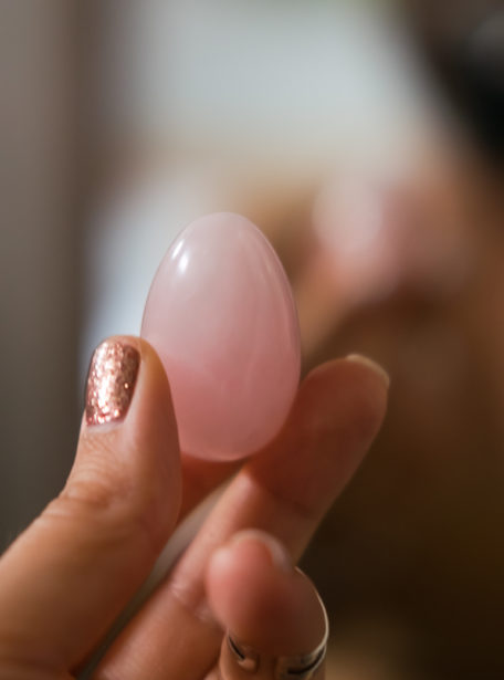 Woman holding in hand a vaginal (yoni) egg. Rose quartz healing crystal egg. Feminine energy concept