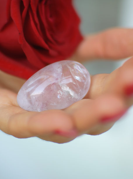 Female hands with manicure holding a yoni egg and red rose. The flower as a symbol of menstruation. Transparent violet amethyst crystal for vumfit, imbuilding or meditation during menstrual cramps.